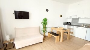 Ein stilvoller, minimalistischer Wohnraum mit Sofa, kleinem Tisch, Fernseher, einer Uhr und einer Topfpflanze.