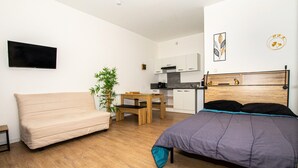 Ein kleines Zimmer mit einem Bett, einem Schlafsofa, einem Esstisch und einer kleinen Küchenzeile.