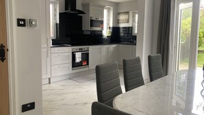 A modern kitchen with white cabinets, a black countertop, and a built-in oven. There is a dining area with a marble table and grey chairs.