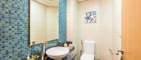 Ein Badezimmer mit blauer Mosaikfliesenwand, einem weißen Waschbecken, einer Toilette und einer Holztür.