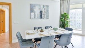 A dining area with a white table set for six, surrounded by blue chairs, a large abstract painting on the wall, and a view of buildings through a window. - Shoreline - Luxury Palm Jumeirah (Dubai)