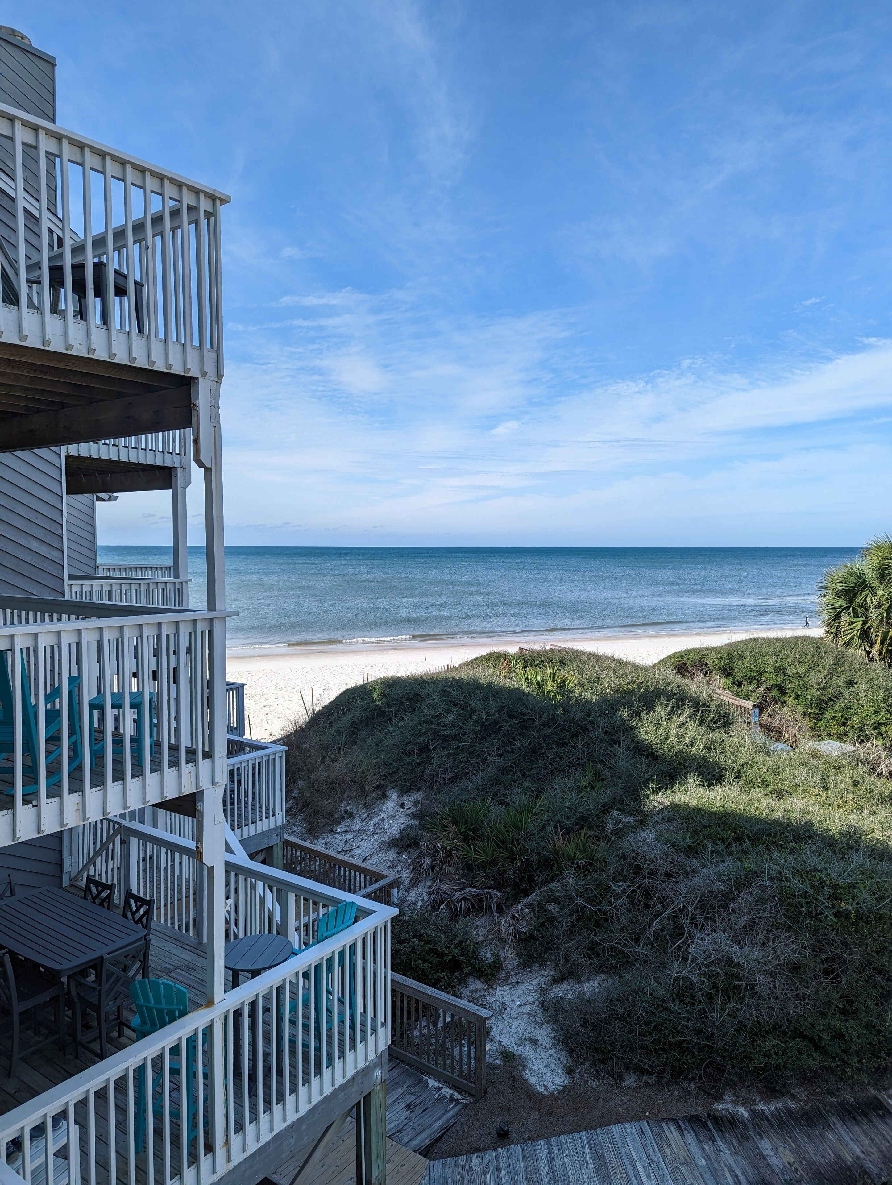 En terrasse i flere niveauer med udendørs møbler, med udsigt over en strand og ocean.