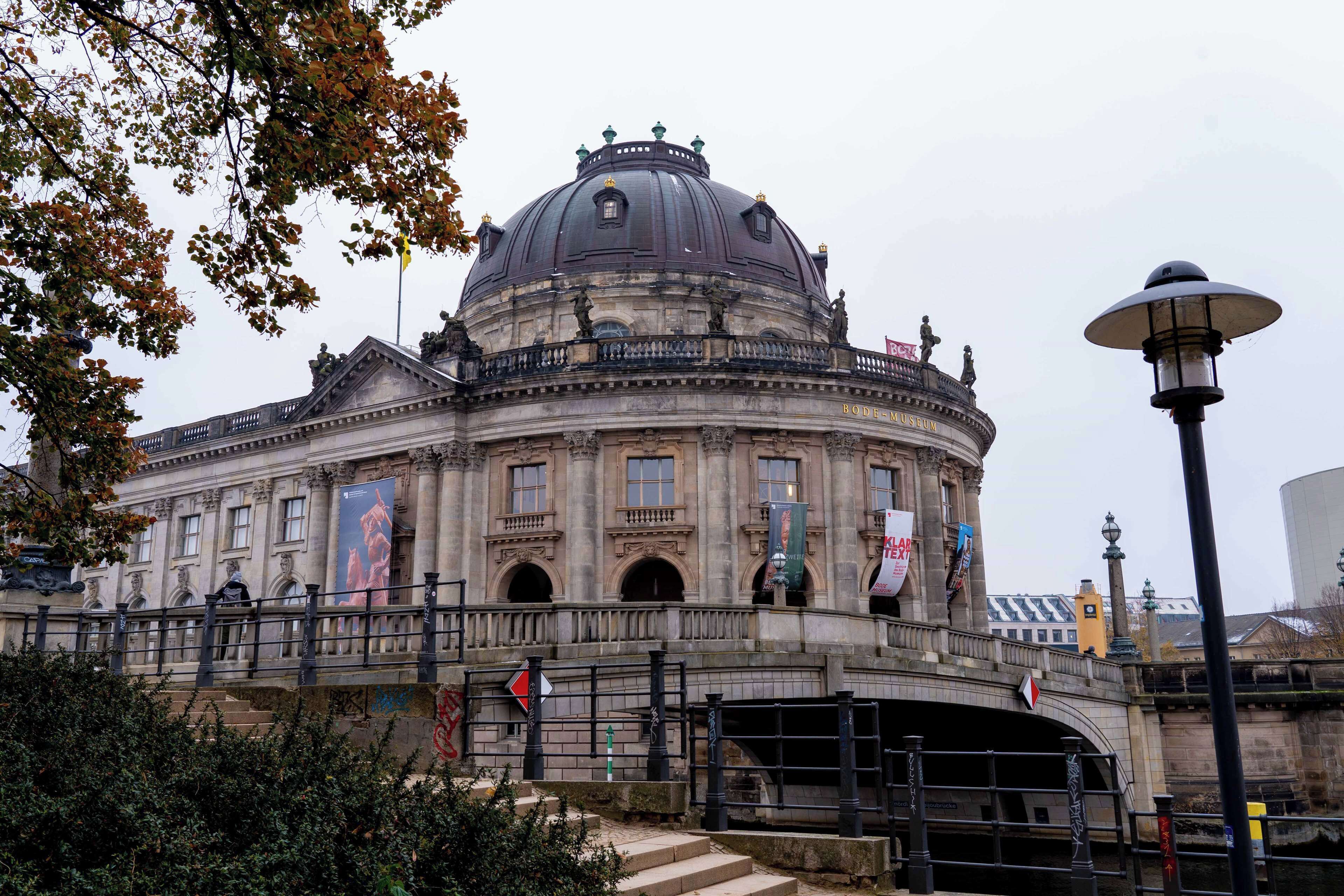 A historic building with a prominent dome, a bridge leading to it, and a lamp post nearby.