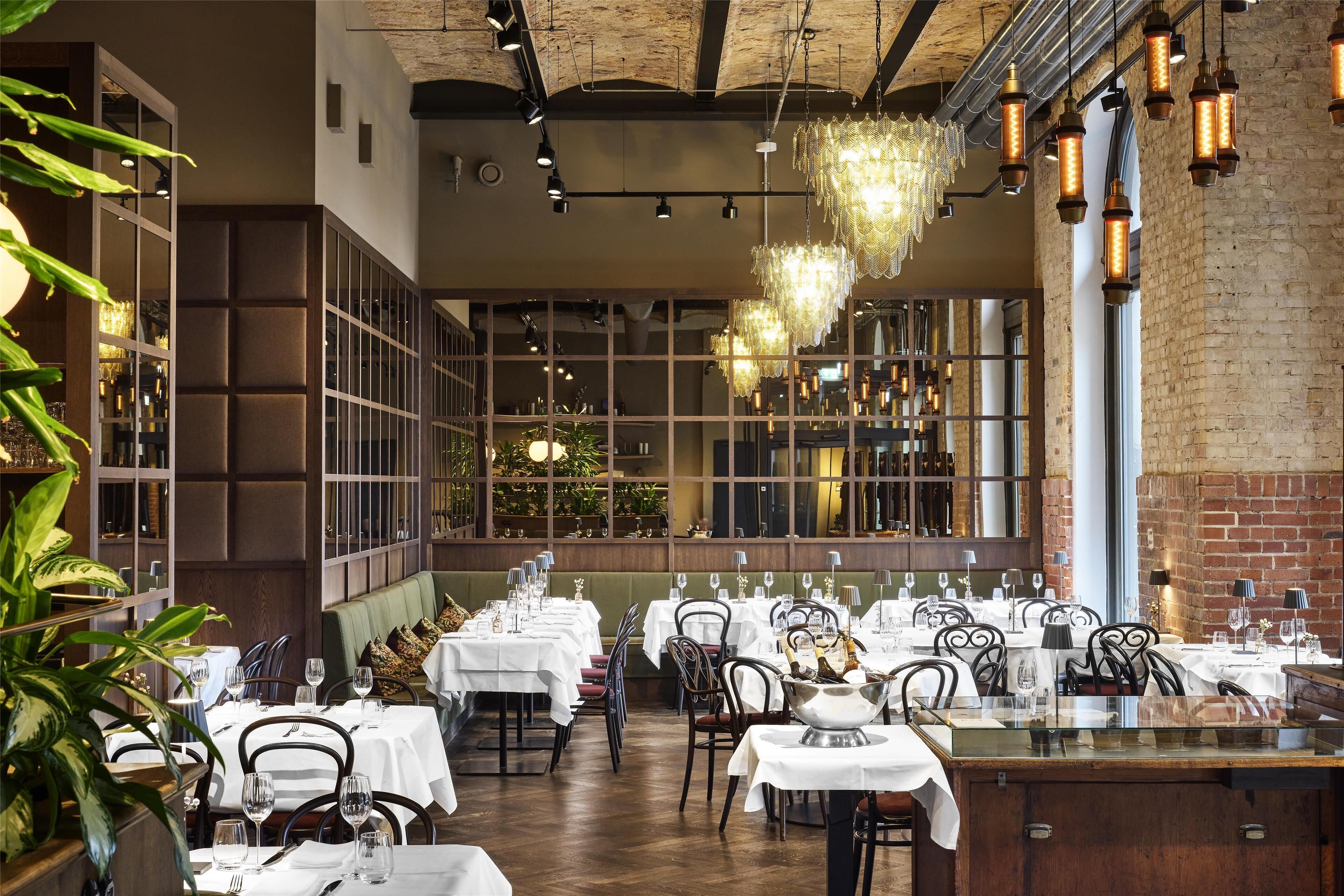 A restaurant with multiple tables set for dining, a brick wall, and hanging lights.