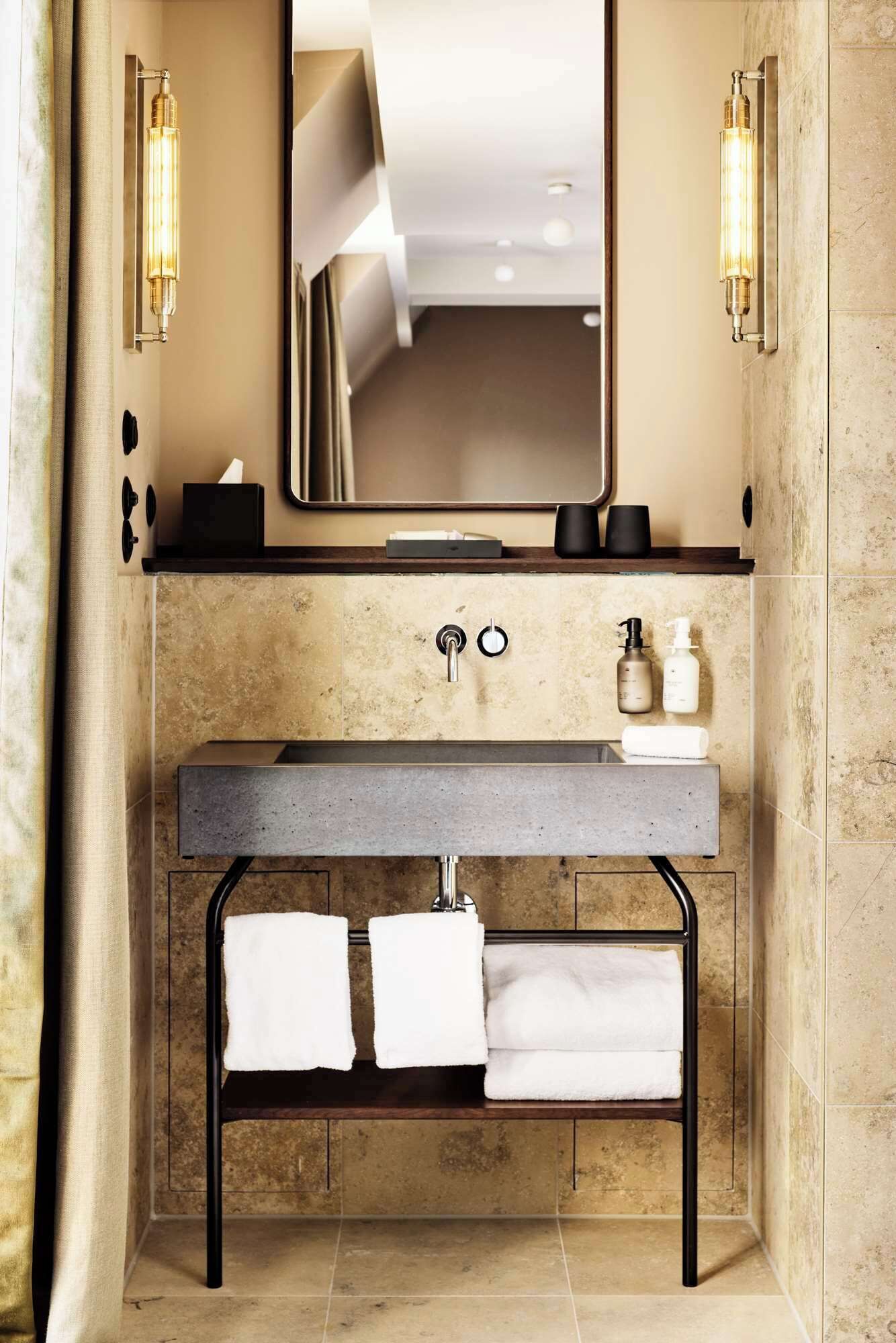 A bathroom with a large mirror, a sink with two faucets, and two towels hanging on a rack.