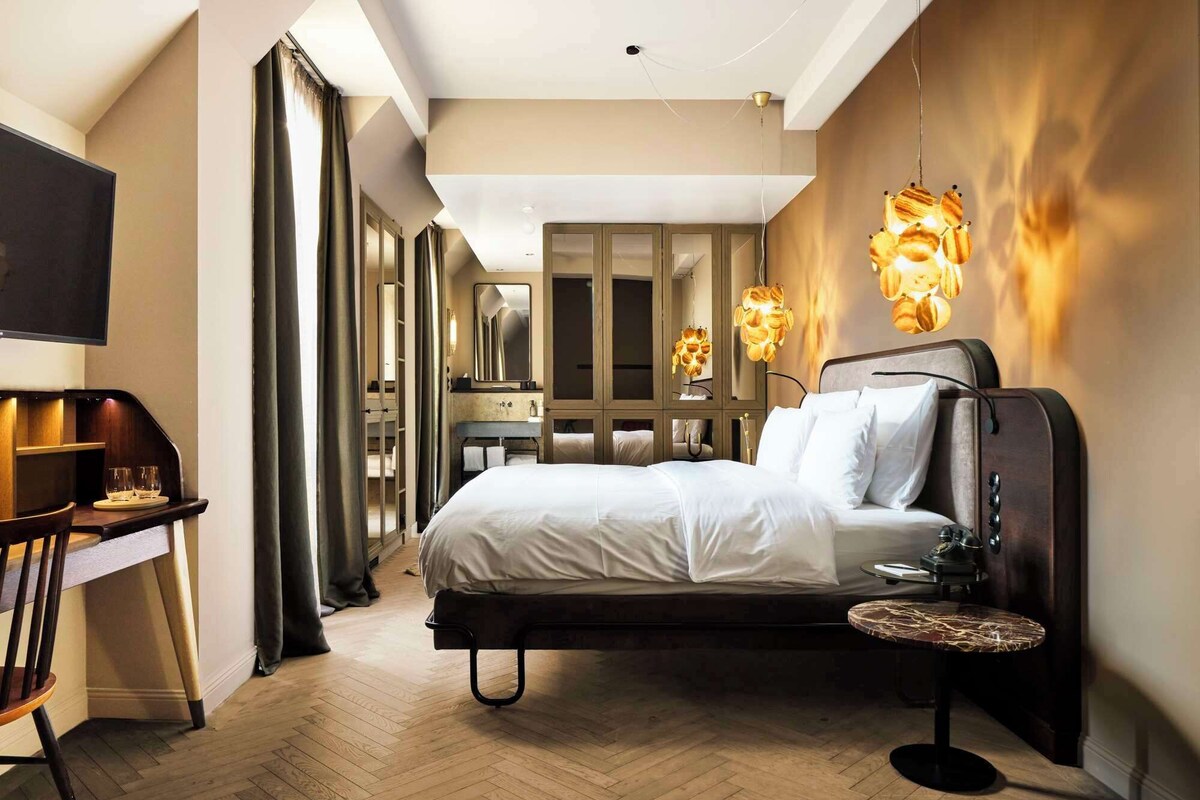 A modern hotel room with a bed, bedside table, and a unique wall-mounted light fixture.