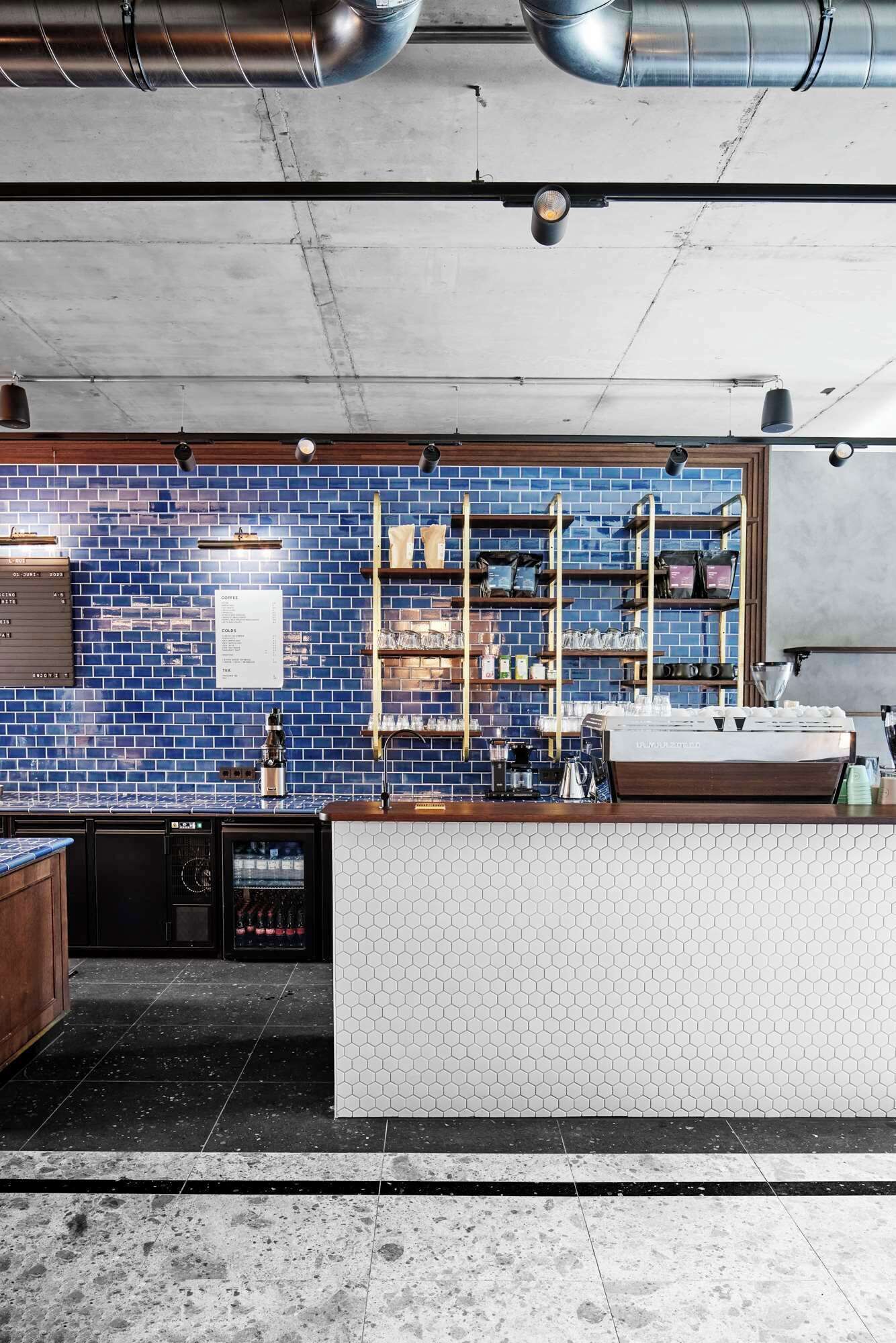 A modern bar with a blue-tiled backsplash, wooden shelves, and a white countertop.