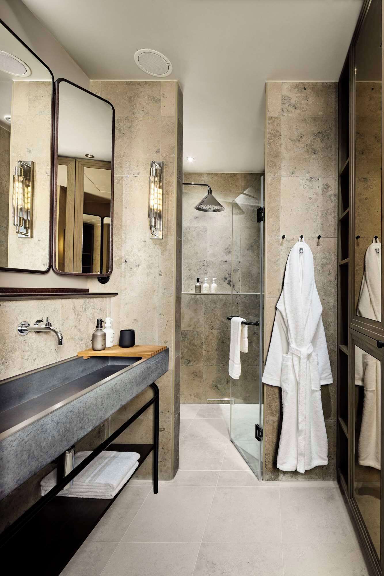 A modern bathroom with a large mirror, a vanity with a sink, a shower area, and a walk-in closet with a robe hanging.