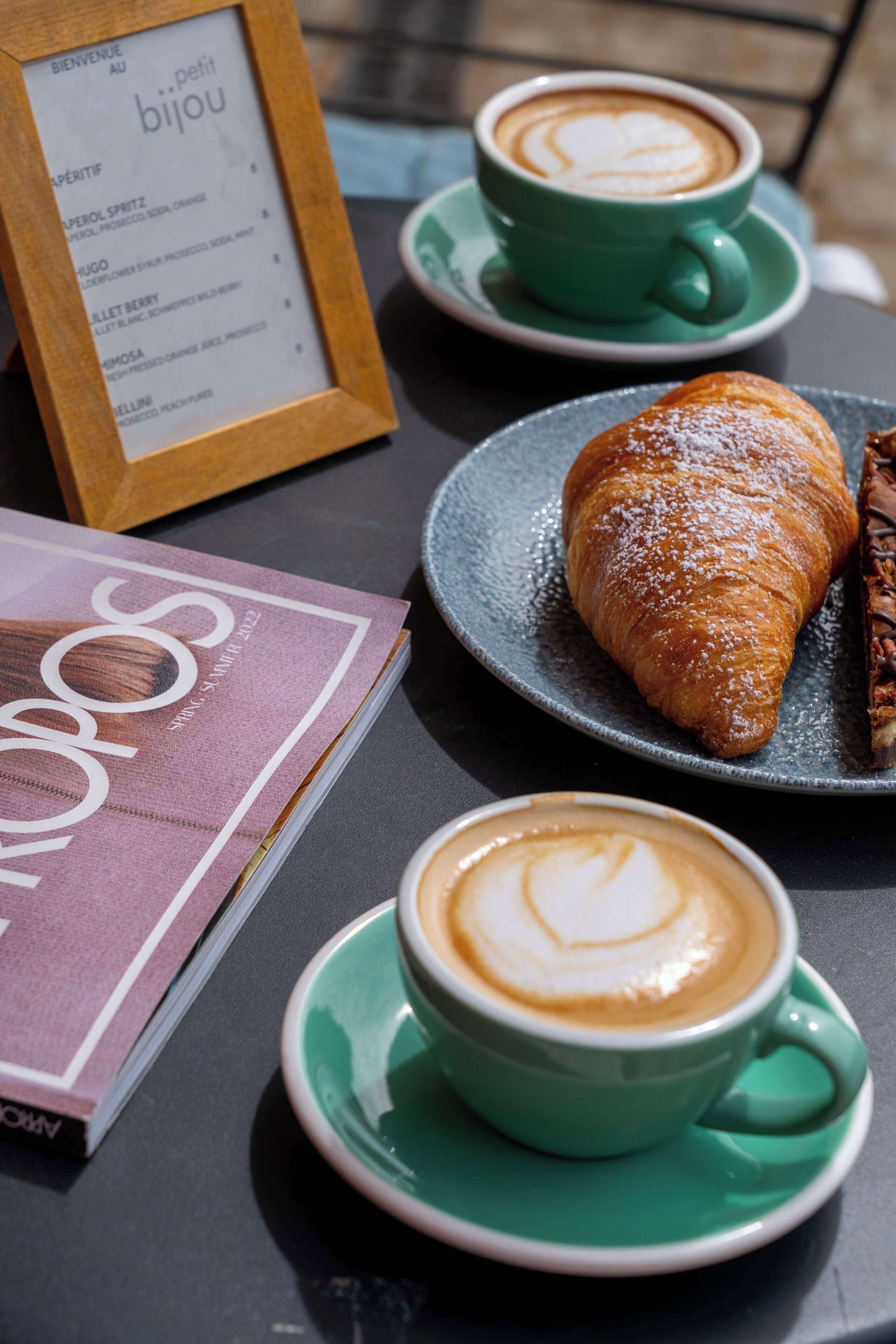 A table with a croissant, two cups of coffee, and a menu.
