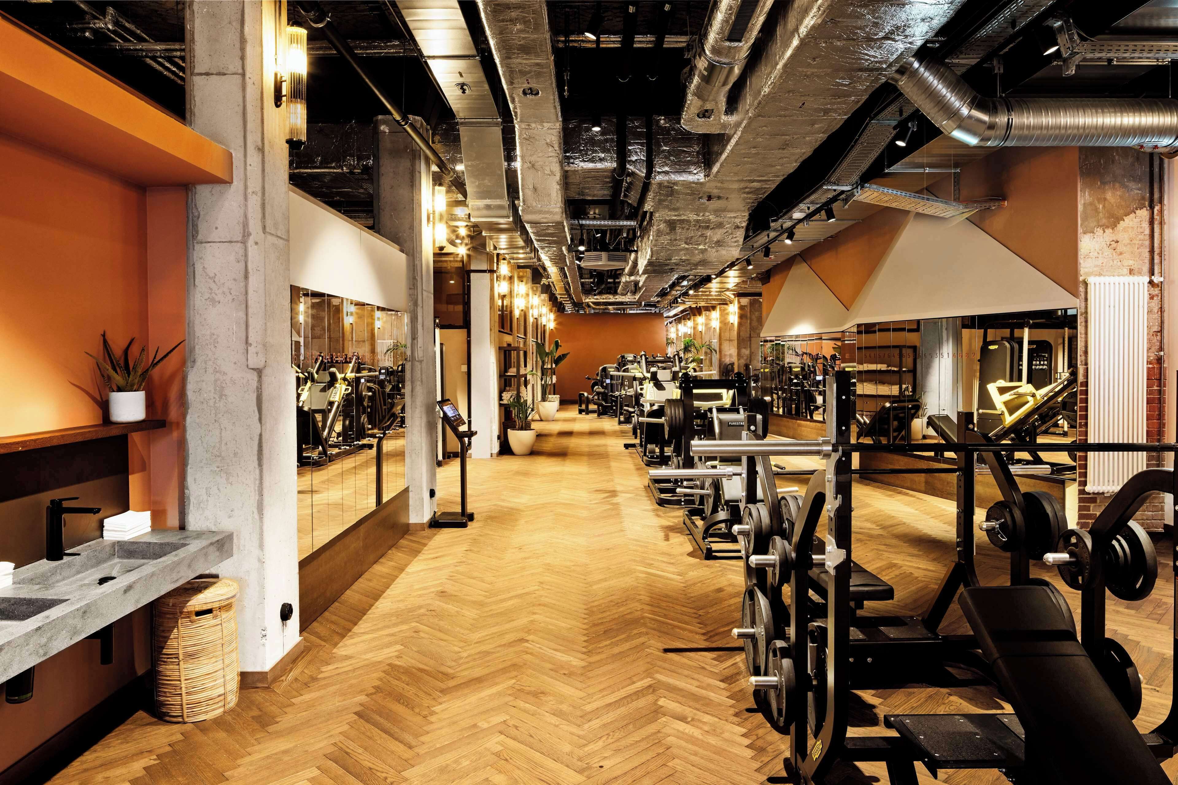 Un gimnasio con suelo de madera, equipo de ejercicio y un pilar de hormigón.
