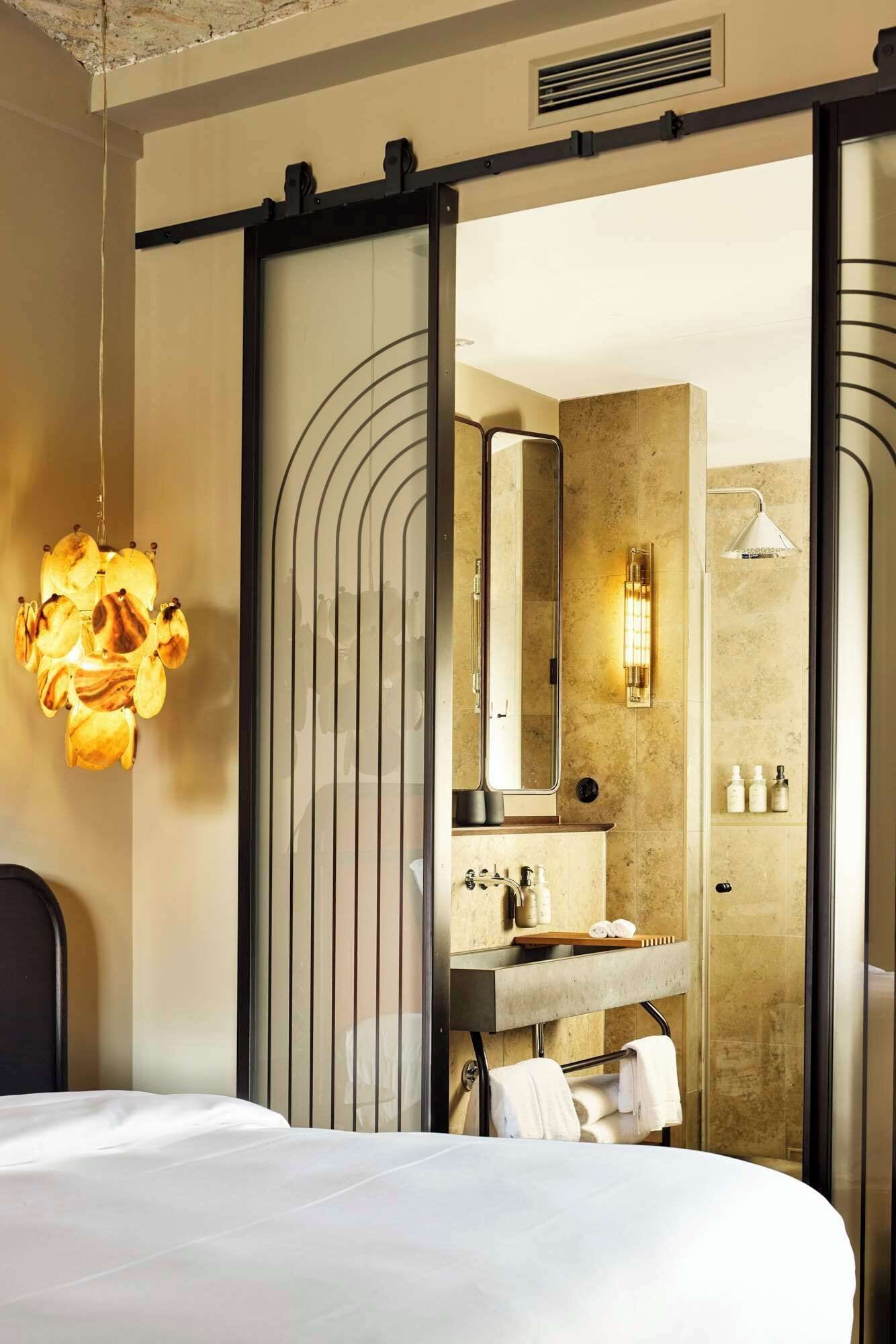 Quarto de hotel moderno com uma cama grande, banheiro com espelho, pia e porta-toalhas.