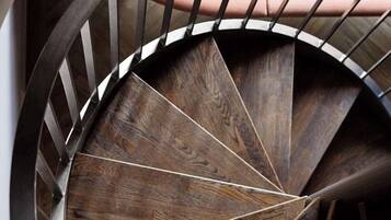 Una escalera de caracol con detalles de madera y barandilla de metal, que conduce a una sala con zona de estar tapizada en tonos rosa.