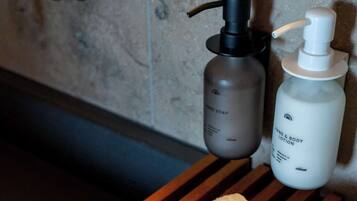 A wooden tray with two white towels, a black pump bottle, and a white bottle of lotion on a bathroom counter.