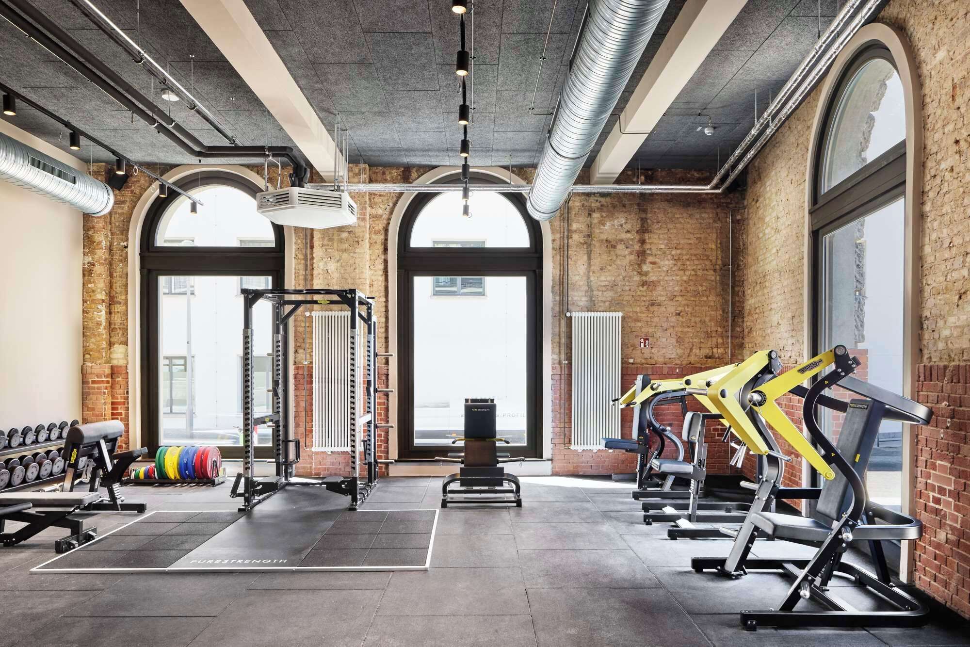 Ett gym med utrustning för styrketräning, löpband och hantlar.
