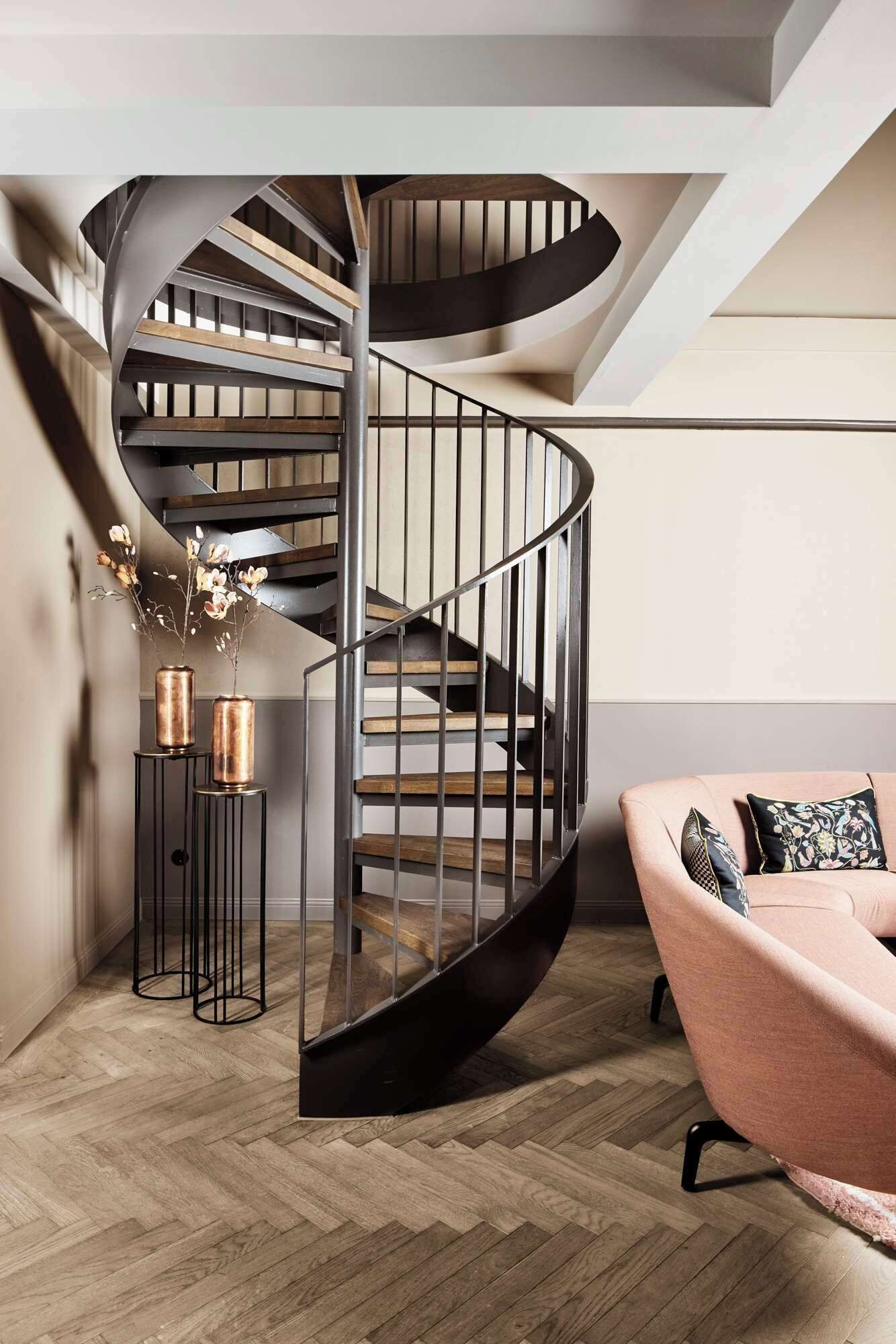 Una escalera espiral moderna con barandillas de metal y peldaños de madera, que conduce a un piso superior.