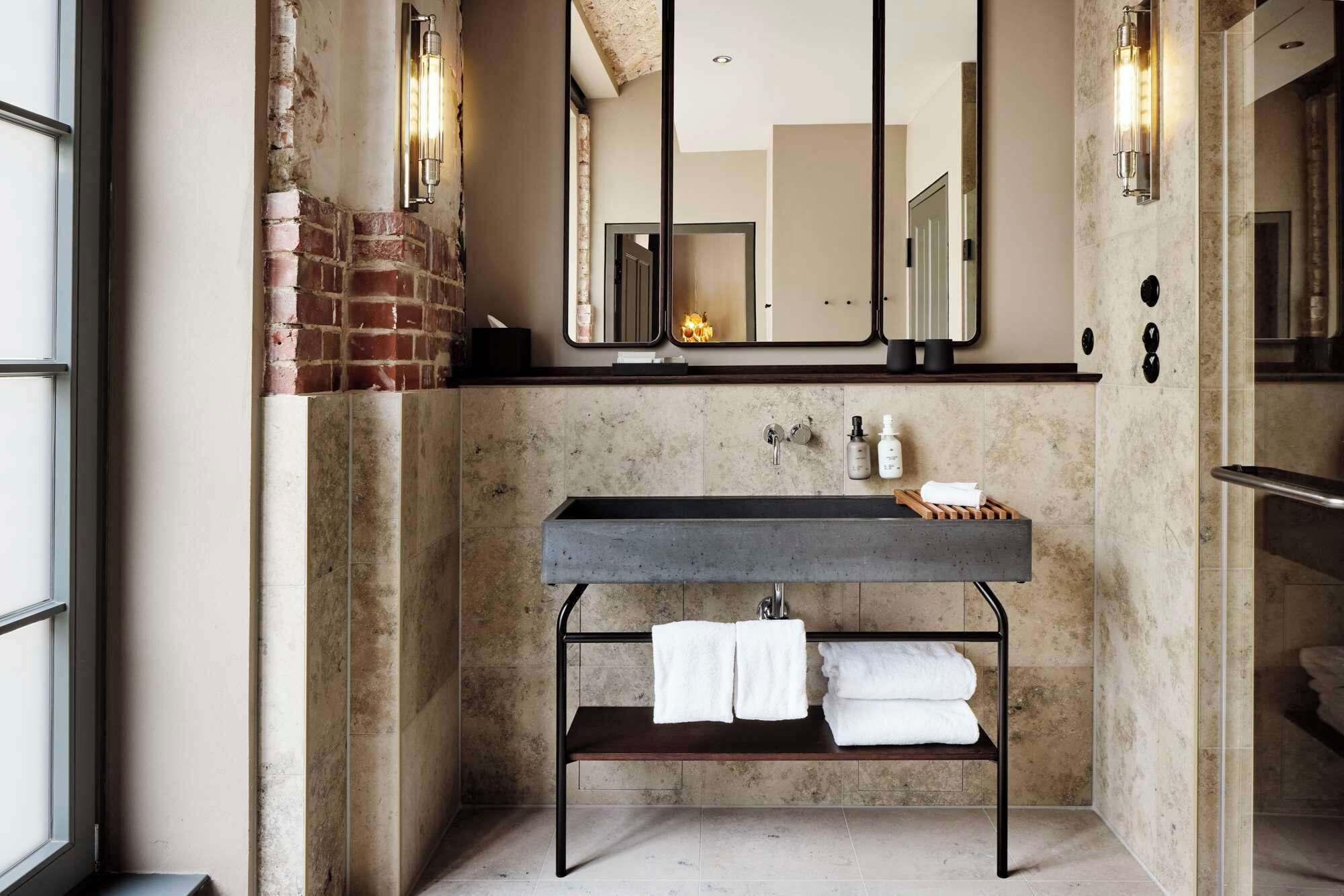 Un baño moderno con pared de piedra, tocador de madera, un espejo y un perchero para toallas.