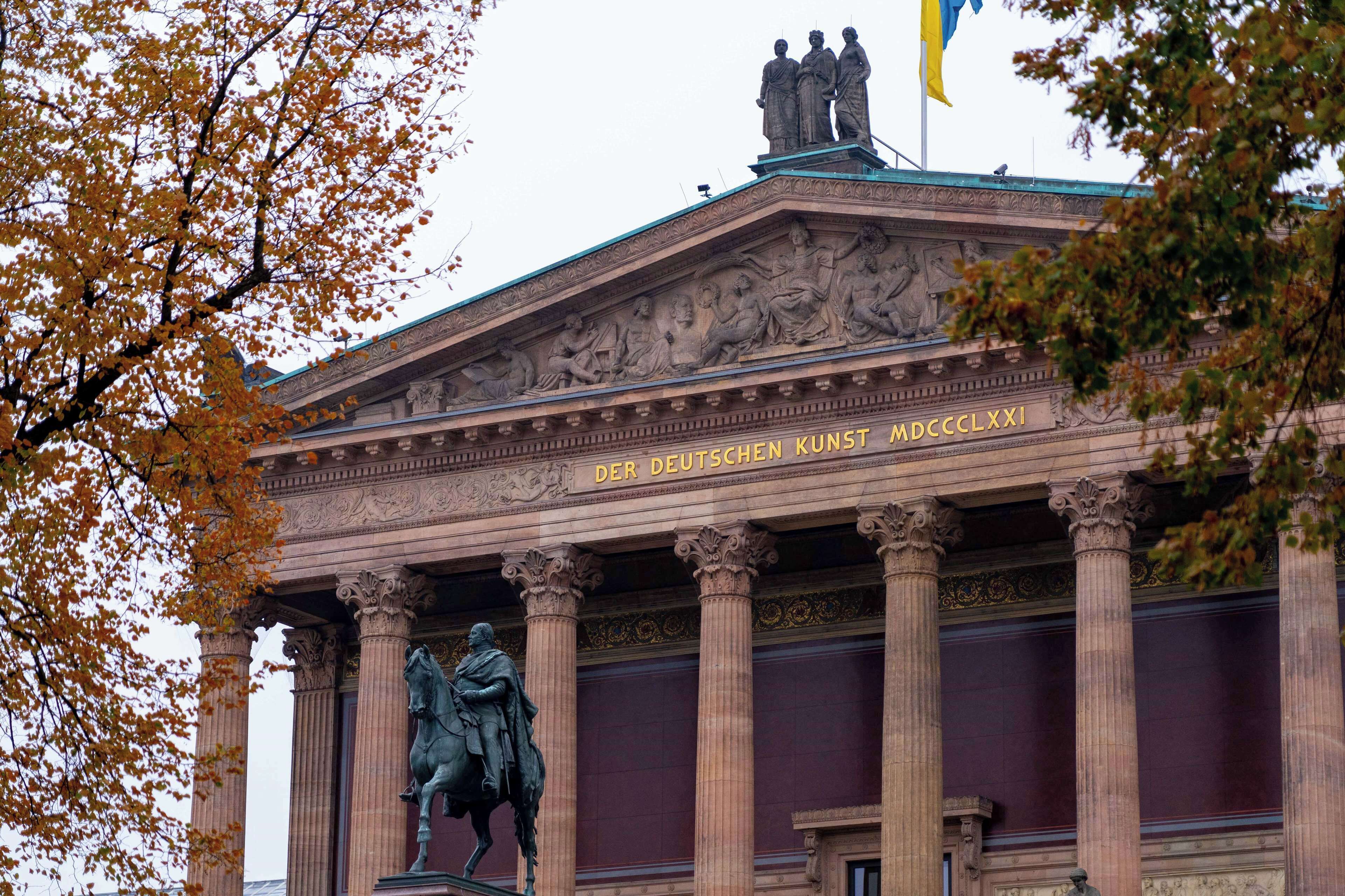 Un edificio neoclásico con columnas, una estatua y una bandera.
