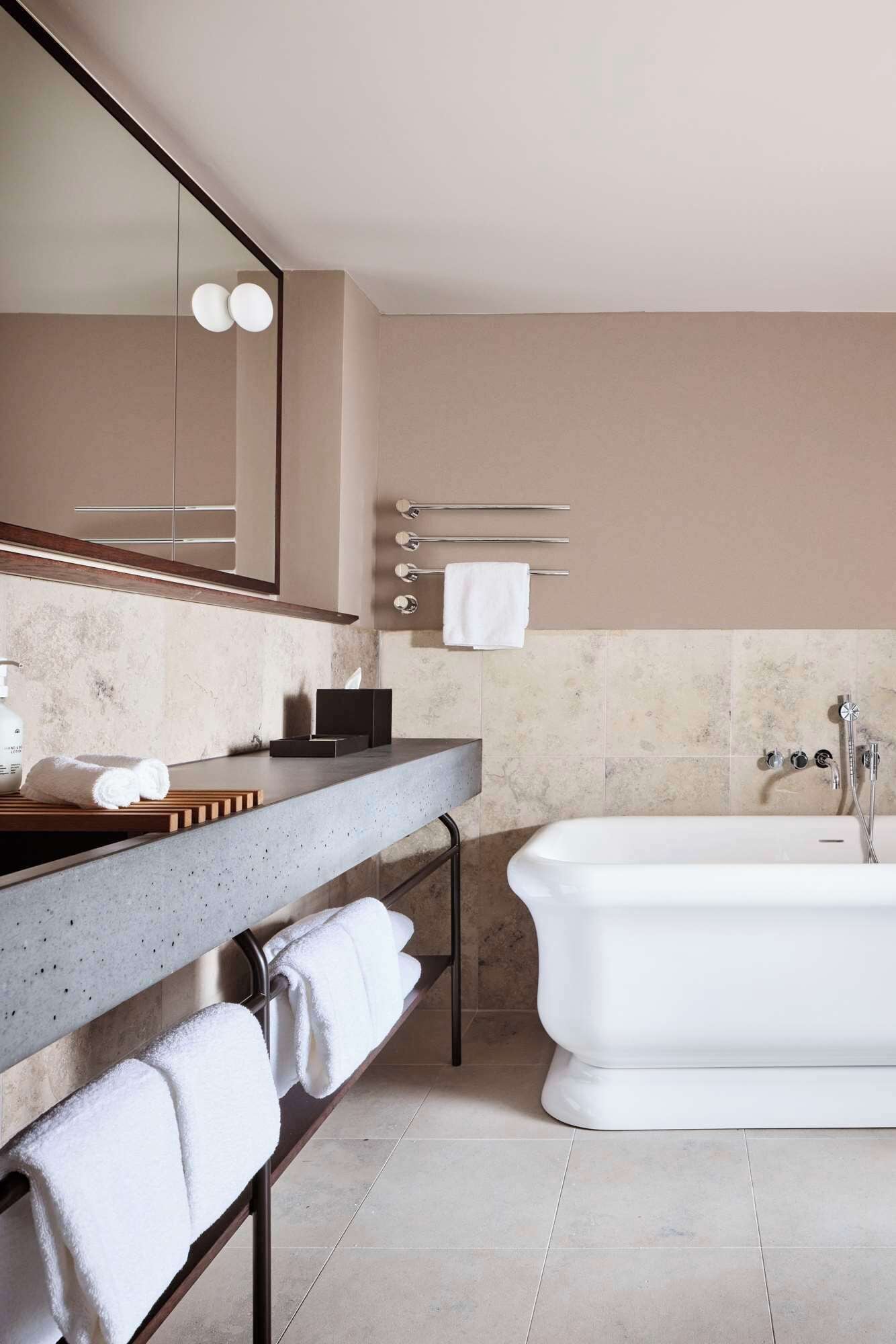 A modern bathroom with a large mirror, a bathtub, and a countertop with a soap dispenser and towel holder.