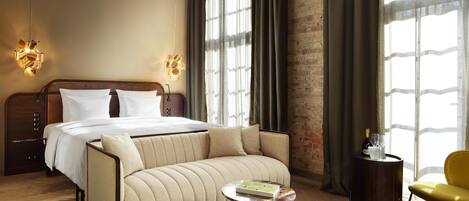 Une chambre d’hôtel avec un lit, un canapé, une table ronde et une petite table d’appoint sur laquelle se trouvent une bouteille et un verre.