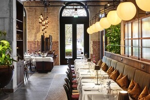 A restaurant with a long dining table, booths, and hanging lights. - Telegraphenamt (Berlin)