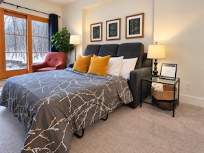 Ein Schlafzimmer mit einem großen Bett, einem roten Sessel, einem Nachttisch mit Lampe und gerahmten Bildern an der Wand.