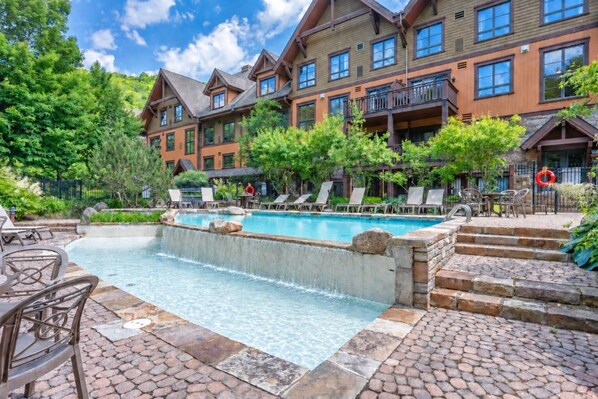 A hotel with a swimming pool, outdoor seating, and a stone pathway.