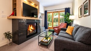 Una sala de estar con chimenea, un sofá, un sillón y una mesa de centro de vidrio.