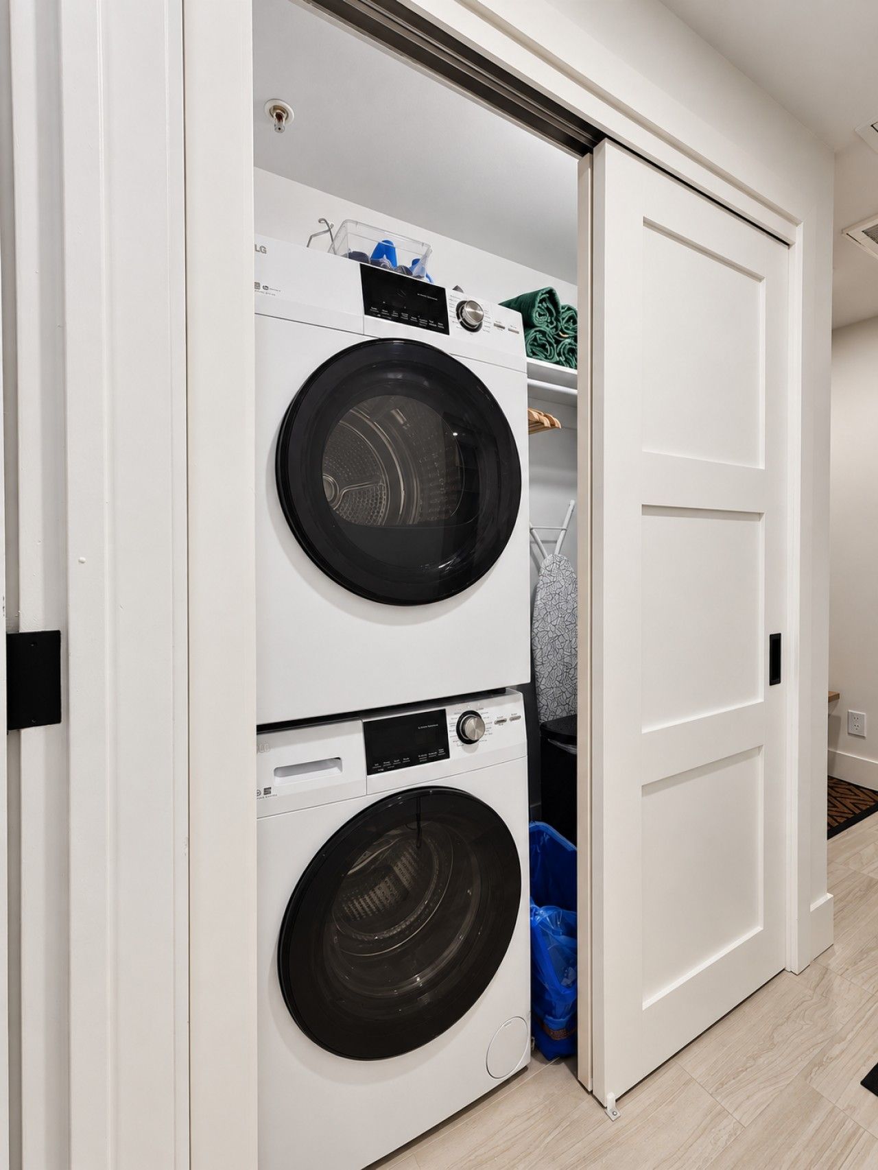 A laundry room with a double washer and dryer, a blue trash bag, and a white door.
