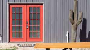 A red door with a grid pattern, a wooden bench, and a large cactus against a corrugated metal wall. - Gorgeous Guesthouse Near Amazing Downtown (San Antonio)