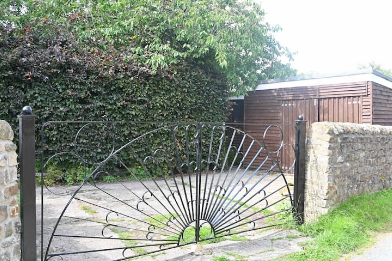 Une porte en métal au motif en éventail, un mur de pierre et un bâtiment en bois en arrière-plan.