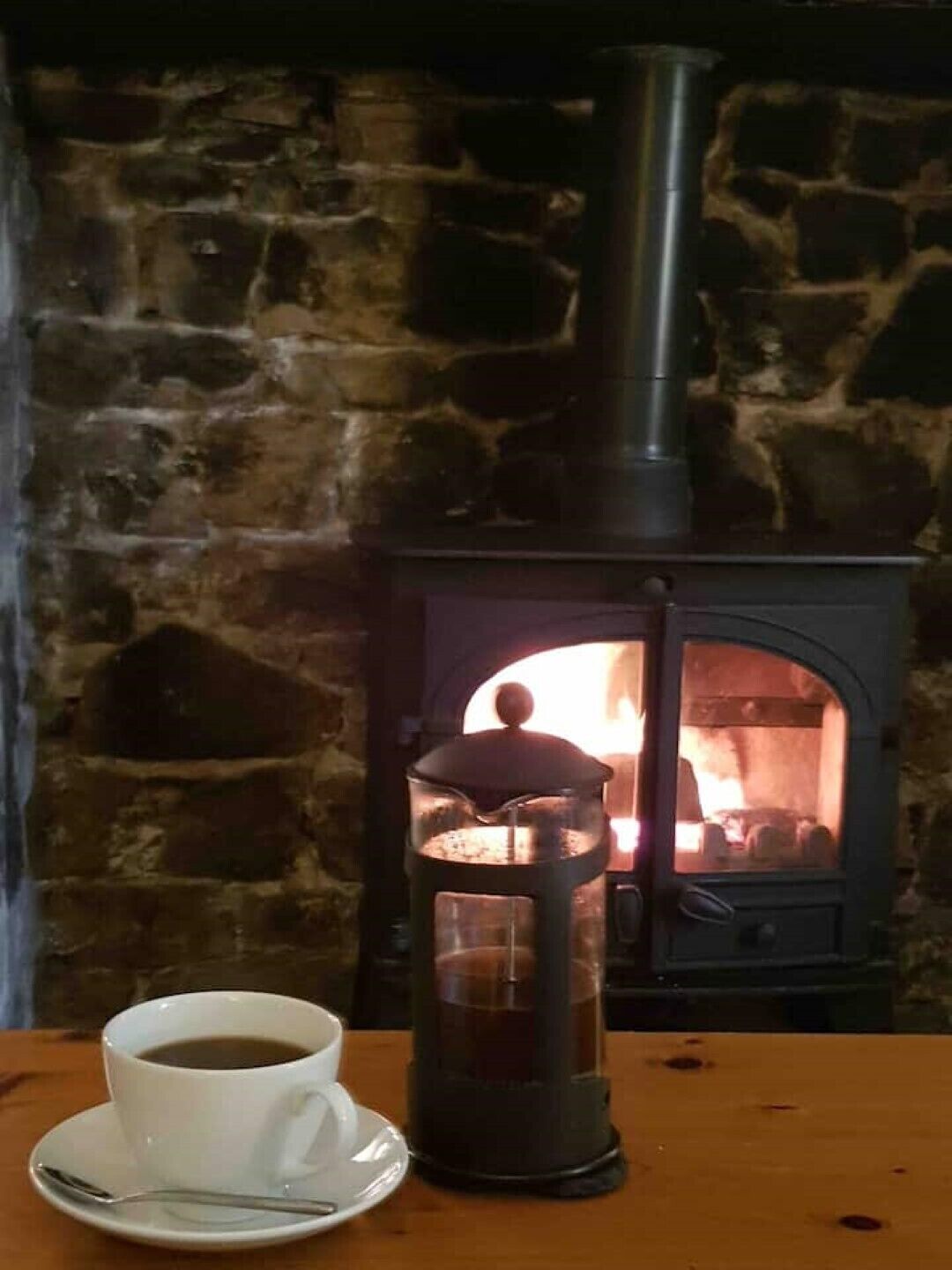 A rustic stone wall, a wood-burning stove, and a cup of coffee on a table.