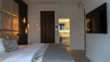 A modern hotel room with a large bed, a flat-screen TV, and a bathroom visible through an open door.