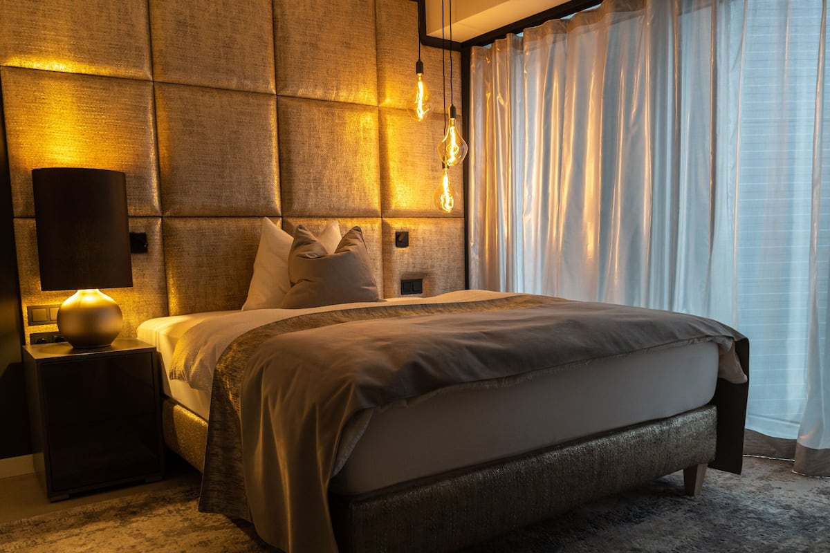 A modern bedroom with a large bed, a nightstand with a lamp, and a wall-mounted light fixture.