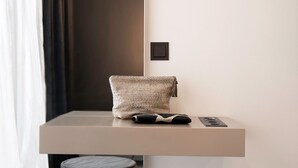 A modern, minimalist room with a neutral color palette, featuring a large window with sheer curtains, a small round ottoman, and a sleek, wall-mounted shelf with a towel and remote control. - THE Newsha Signature Home (Muelheim an der Ruhr)