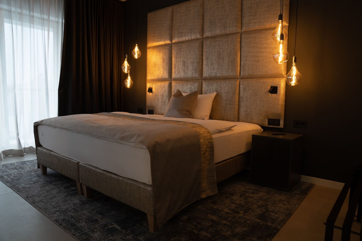 A modern bedroom with a large bed, a headboard with a textured panel, and two bedside lamps.
