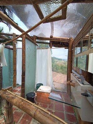 Un baño rústico con estructura de bambú, zona de ducha y vistas al paisaje.