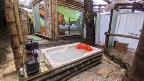 A hot tub with a bamboo structure and a small table with a kettle and a glass. - Biohotel Ecohouse (Guarne)