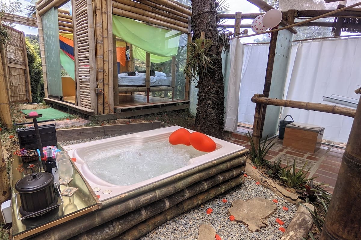 A hot tub with a bamboo structure and a small table with a kettle and a glass.