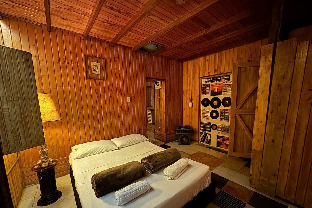 A wooden-paneled room with a bed, a lamp, a record player, and a wall display of vinyl records.