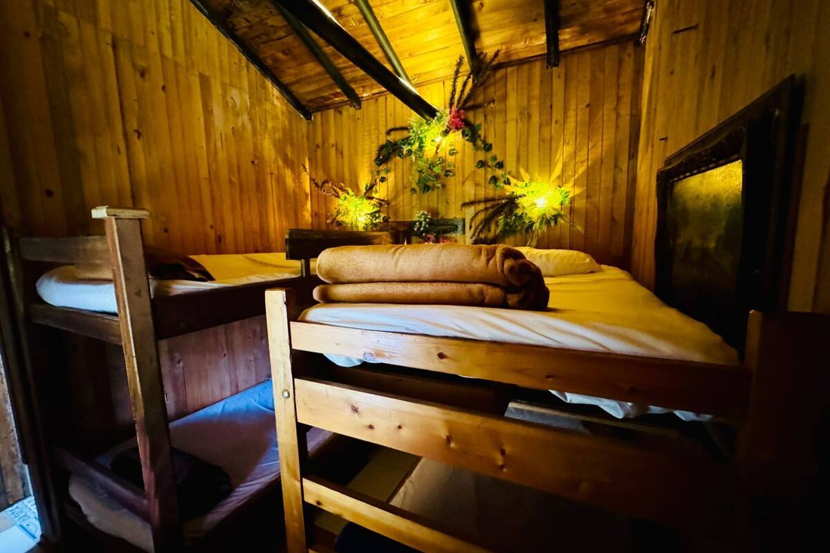 A wooden cabin room with a bunk bed, a small desk, and a chair. There are two flower arrangements on the bed.