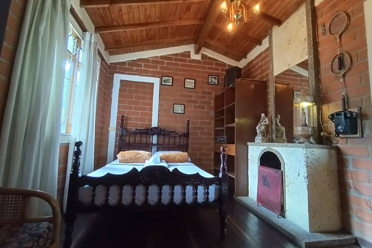 A bedroom with a wooden ceiling, a brick wall, a bed with a headboard, a dresser, and a mirror.