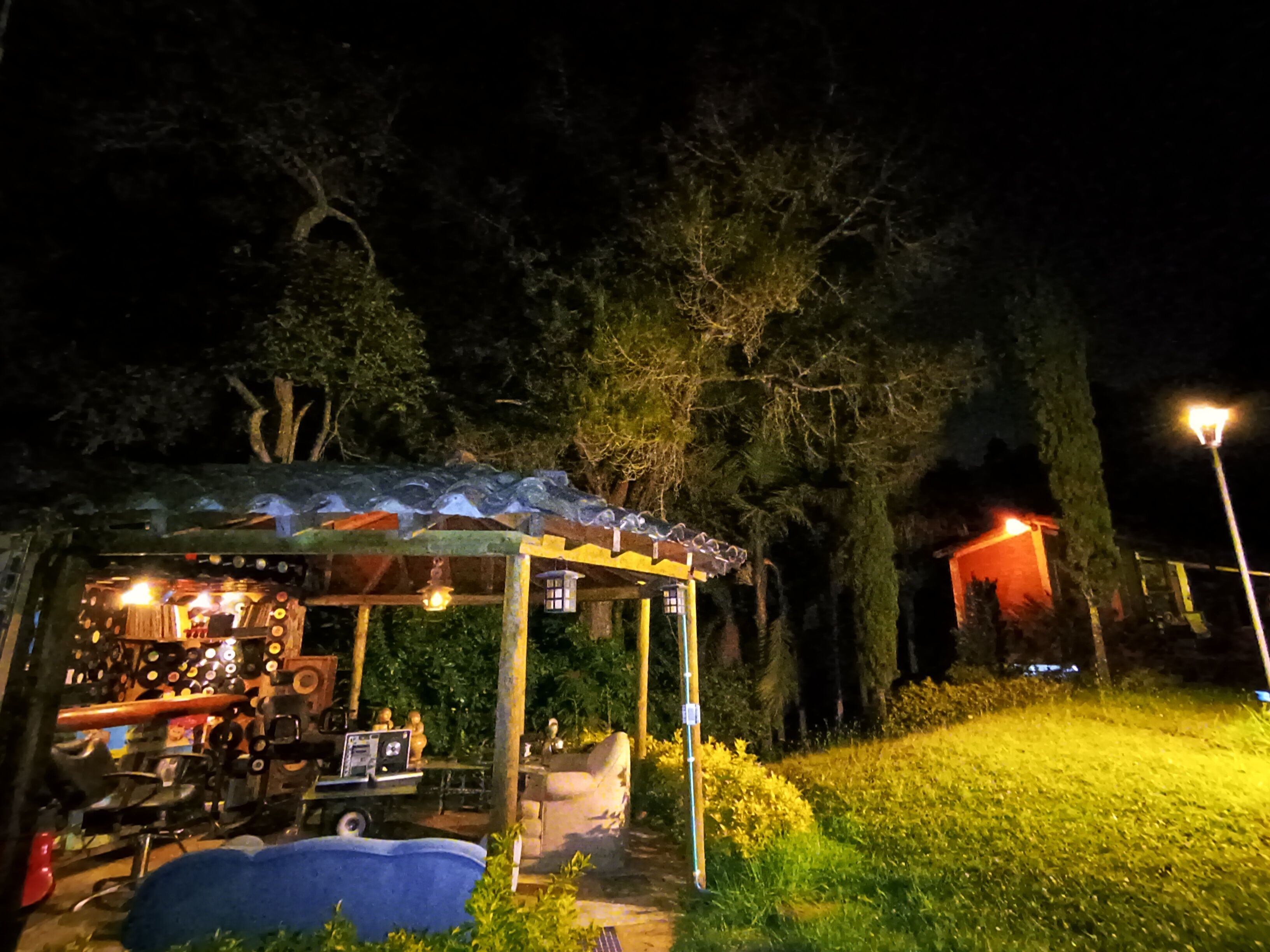Una pequeña estructura al aire libre con un área de estar techada, una mesa con varios objetos y un elemento azul en el suelo.