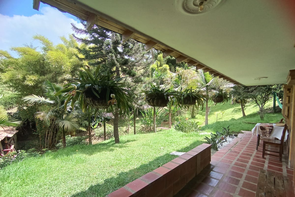 A covered outdoor area with a brick floor, a wooden bench, and hanging planters.