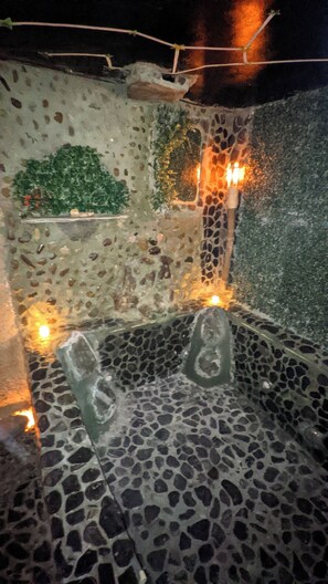 A stone-tiled bathroom with a mosaic wall and two illuminated candles. - Biohotel Ecohouse (Guarne)
