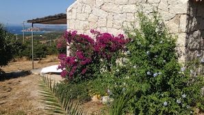 Un bâtiment en pierre, surmonté d’un toit en tuiles, entouré d’une végétation luxuriante et de fleurs aux couleurs vives.