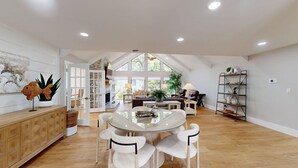A spacious living area with a high ceiling, a glass dining table surrounded by chairs, a fireplace, and a large window providing natural light. - New to the Rental Market! (Hilton Head)