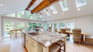 A spacious kitchen with a large island, wooden ceiling beams, and large windows offering views of greenery. - New to the Rental Market! (Hilton Head)