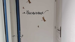 A hallway with a white wall featuring a 'Bienvenue' sign and decorative dragonfly stickers.