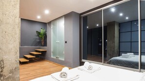 Een moderne hotelkamer met een grote schuifglazen deur, een houten trap, een potplant en een bed met handdoeken.