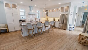 A modern kitchen with white cabinetry, a central island with bar stools, stainless steel appliances, and a herringbone-patterned backsplash. - Bright, Airy Beachwalk Resort w/Golf Cart (Michigan City)